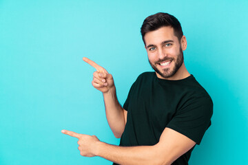 Caucasian handsome man isolated on blue background pointing finger to the side and presenting a product