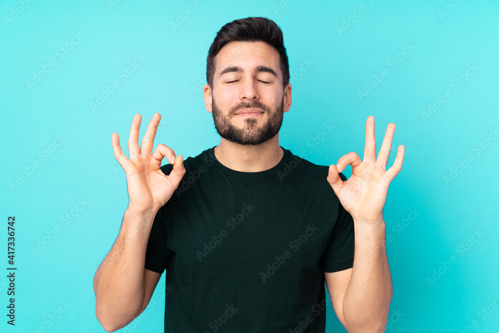 Fototapeta premium Caucasian handsome man isolated on blue background in zen pose