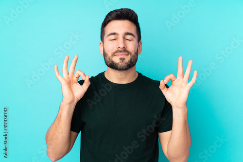 Caucasian handsome man isolated on blue background in zen pose