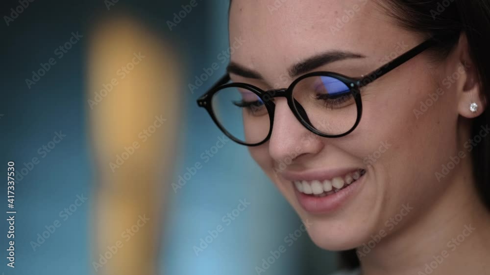 A close-up view of a smiling young woman wearing glasses is using her laptop while sitting at the apartments A close-up view of a smiling young woman wearing glasses is using her laptop while sitting at the apartments