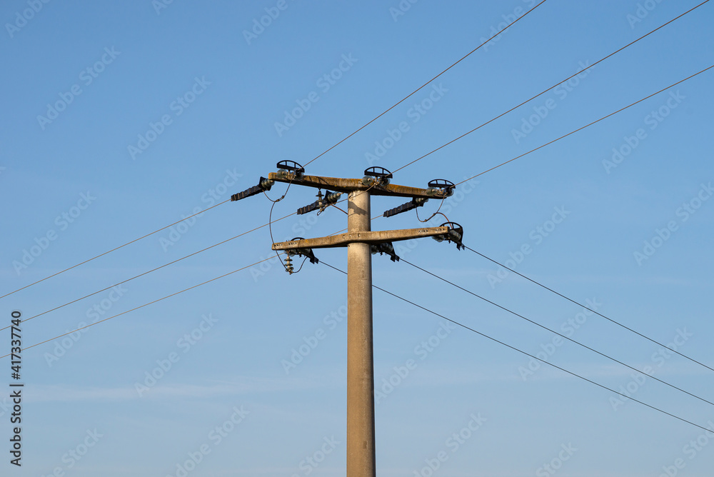 Concrete electric pole with ceramic insulators and voltage lines, in background blue sky with blue sky.