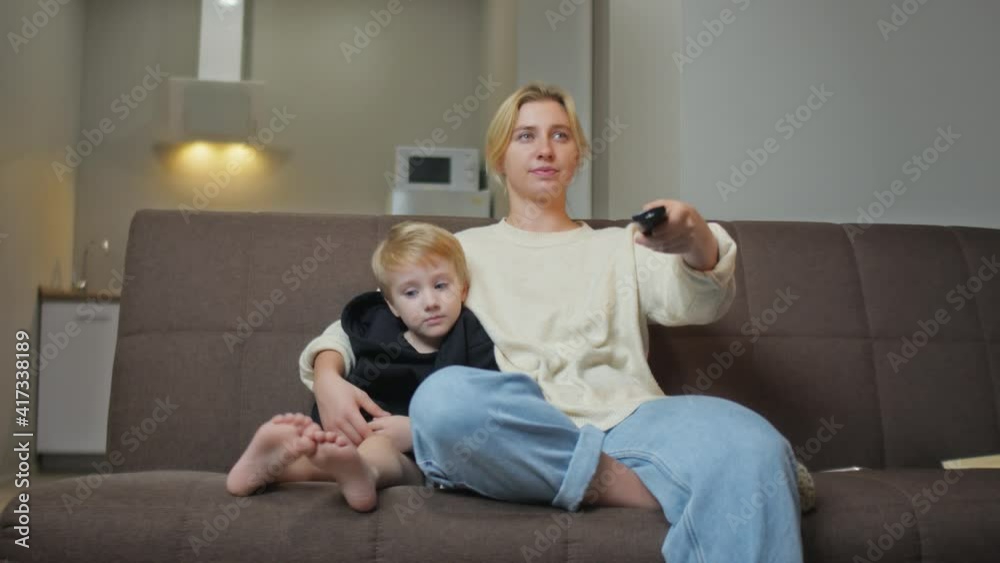 Young mother sits with her son on couch and watch TV Young mother sits with her son on couch and watch TV