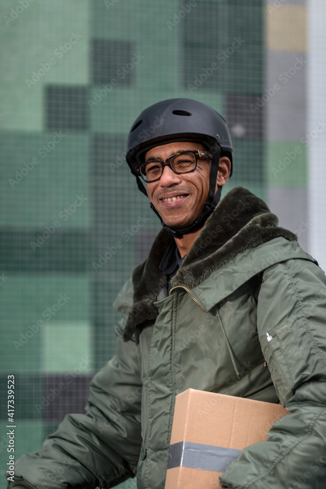 Smiling bicycle courier holding cardboard box Smiling bicycle courier holding cardboard box