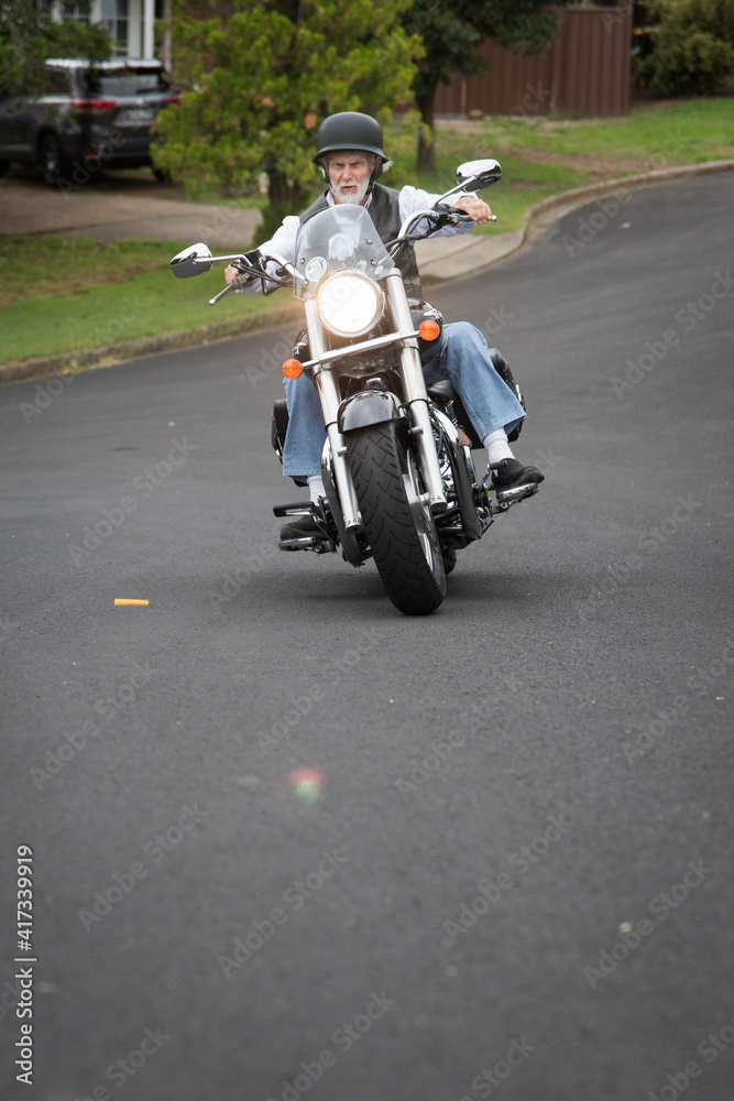 View of a male active senior man riding his bike looking down at the handlebars of his motorbike cycle chrome guages mirros hand instrumentation outdoors on a bright day View of a male active senior man riding his bike looking down at the handlebars of his motorbike cycle chrome guages mirros hand instrumentation outdoors on a bright day