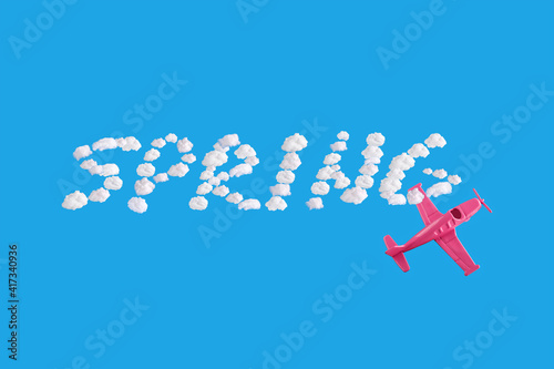 Pink airplane goes into a sharp turn on blue background and word spring of abstract shapes of cloud. Minimal composition. Transportation, travel or vacation concept