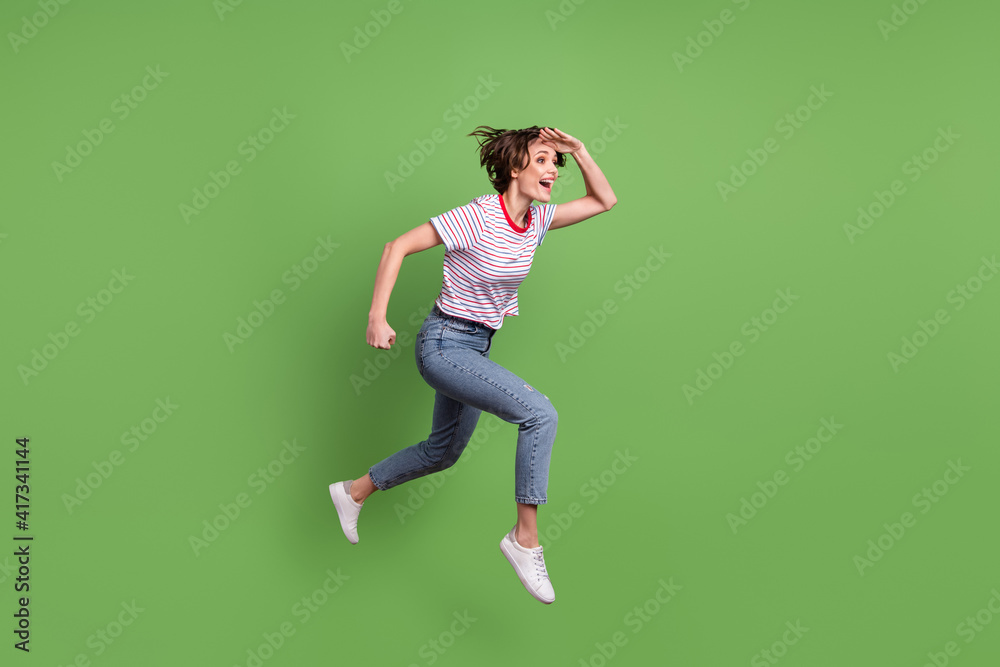 Full length body size profile side view of attractive cheerful girl jumping running search isolated over green pastel color background Full length body size profile side view of attractive cheerful girl jumping running search isolated over green pastel color background