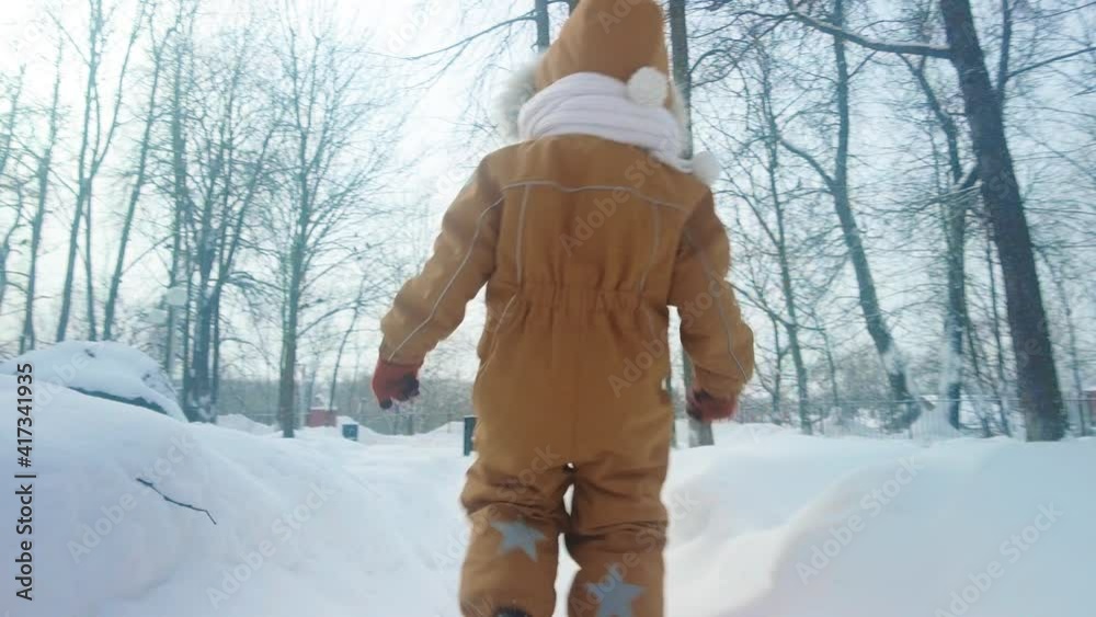 Slow motion shot of a little girl in warm orange clothes walking in the snow after heavy snowfall Slow motion shot of a little girl in warm orange clothes walking in the snow after heavy snowfall