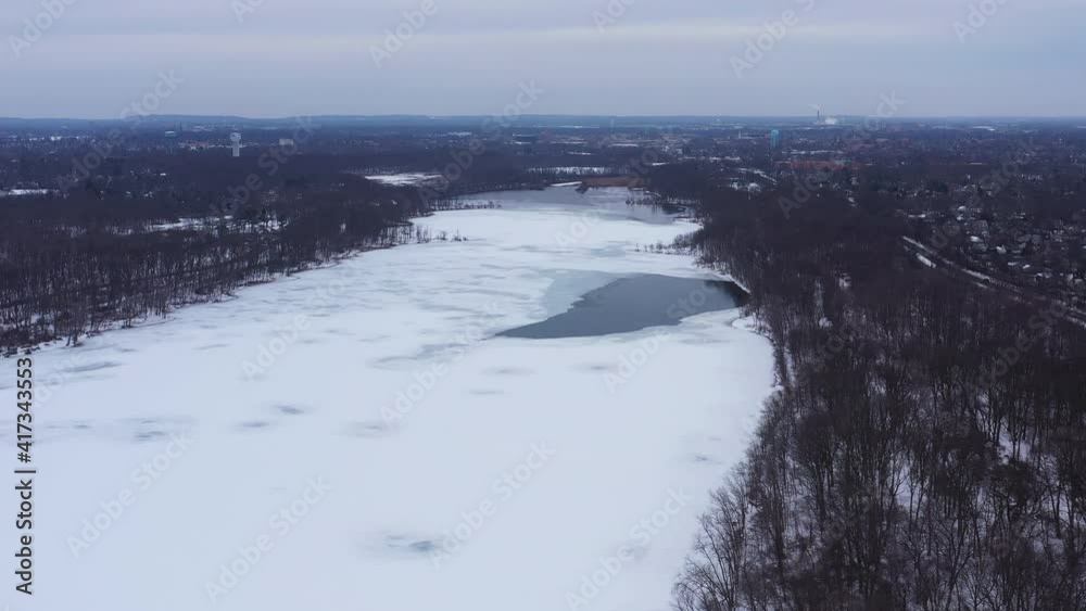 An aerial view from a drone, over a frozen lake during sunrise on a cloudy morning. The camera truck right and boom up over the trees with snow covering the frozen lake in view. An aerial view from a drone, over a frozen lake during sunrise on a cloudy morning. The camera truck right and boom up over the trees with snow covering the frozen lake in view.