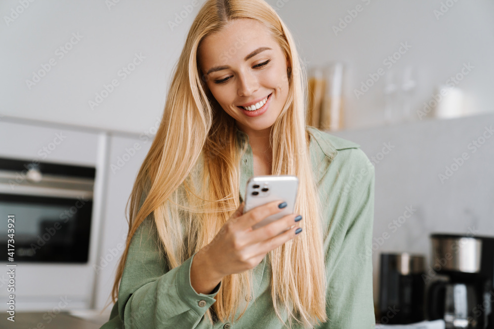 Happy blonde woman using cellphone at home kitchen Happy blonde woman using cellphone at home kitchen