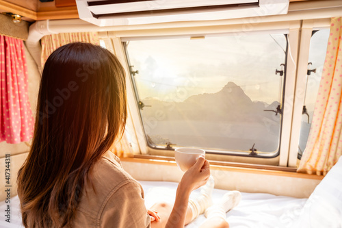 Young woman traveler with cup of coffee laying in camper van and looking beautiful landscape while road trip traveling on vacation