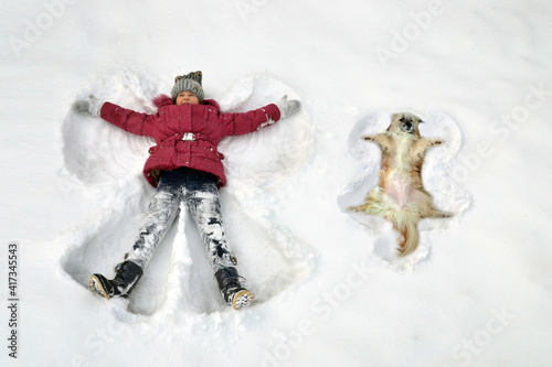Kid in theSnow in Winter makes a Snow Angel together with a dog