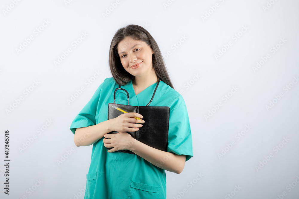 Photo of a young female doctor standing with notebook and pencil Photo of a young female doctor standing with notebook and pencil