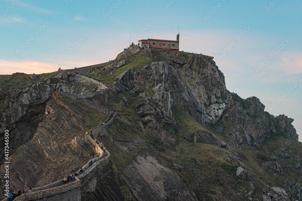 Hermitage of San Juan de Gaztelugatxe seen from afar, people climbing the stairs up the hill to reach the top