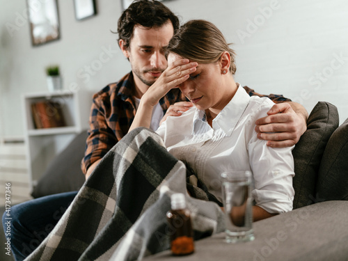Fototapeta Naklejka Na Ścianę i Meble -  Young woman sick in bed. .Woman drinking medicine, having stomach pain. Husband and wife sitting on sofa.