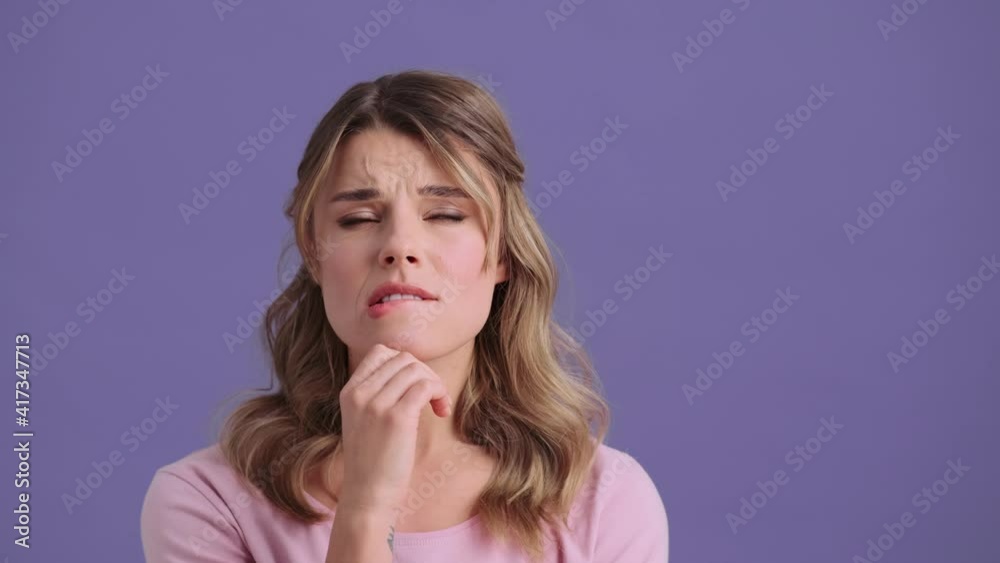 A serious young woman is thinking about something standing isolated over violet wall in the studio A serious young woman is thinking about something standing isolated over violet wall in the studio