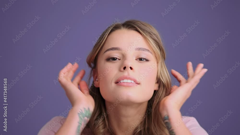 A pleased young woman is looking to the mirror at her face standing isolated over gray wall in the studio A pleased young woman is looking to the mirror at her face standing isolated over gray wall in the studio