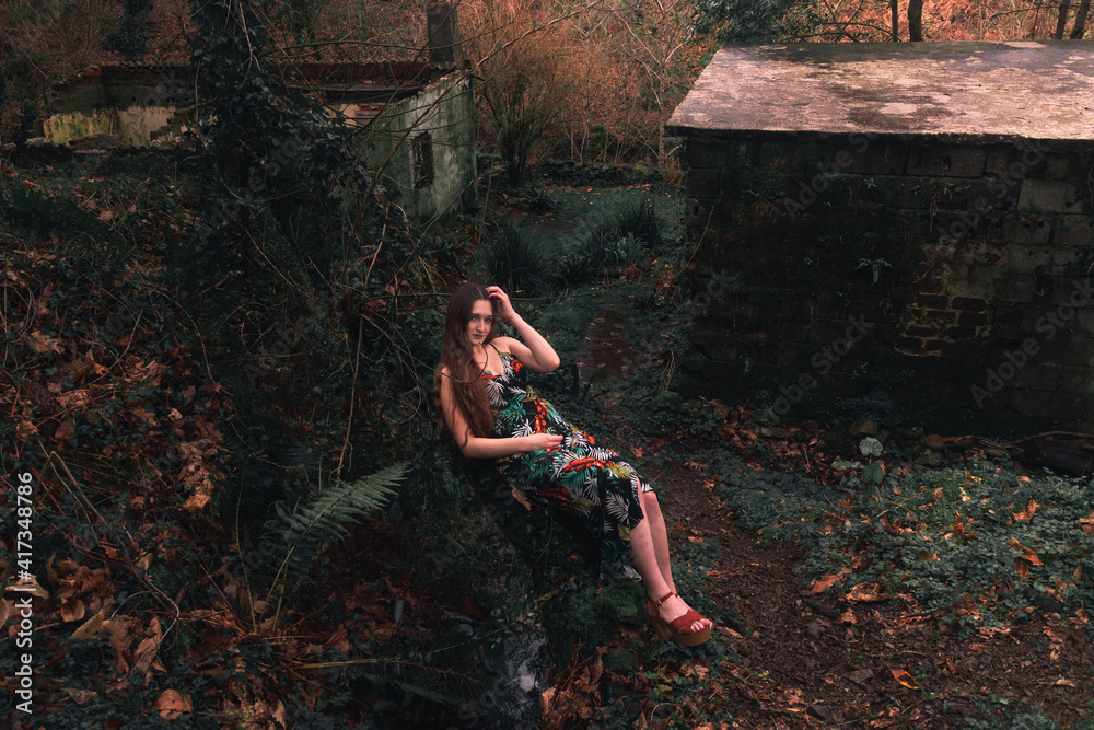 Young caucasian woman with a colorful dress in the middle of the forest next to a little river