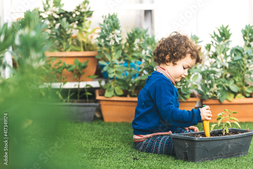 Nice adorable little girl playing in the backyard garden with plants and pots.