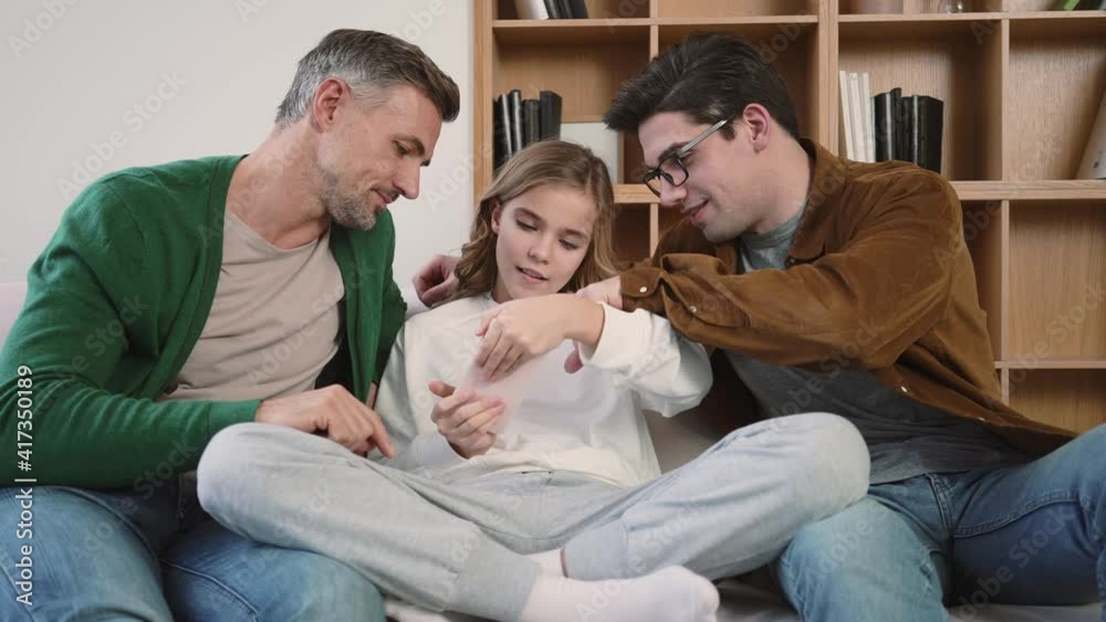Happy gay family are using mobile phone while sitting on couch at home