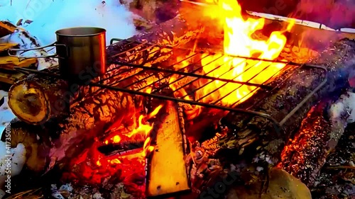 manmade log cabin style firepit with a metal gril on it boiling hot chocolate coffee steaming out with viger fire flaming with wooden plywood planks fed into the fire on a winter snow covered grounds photo