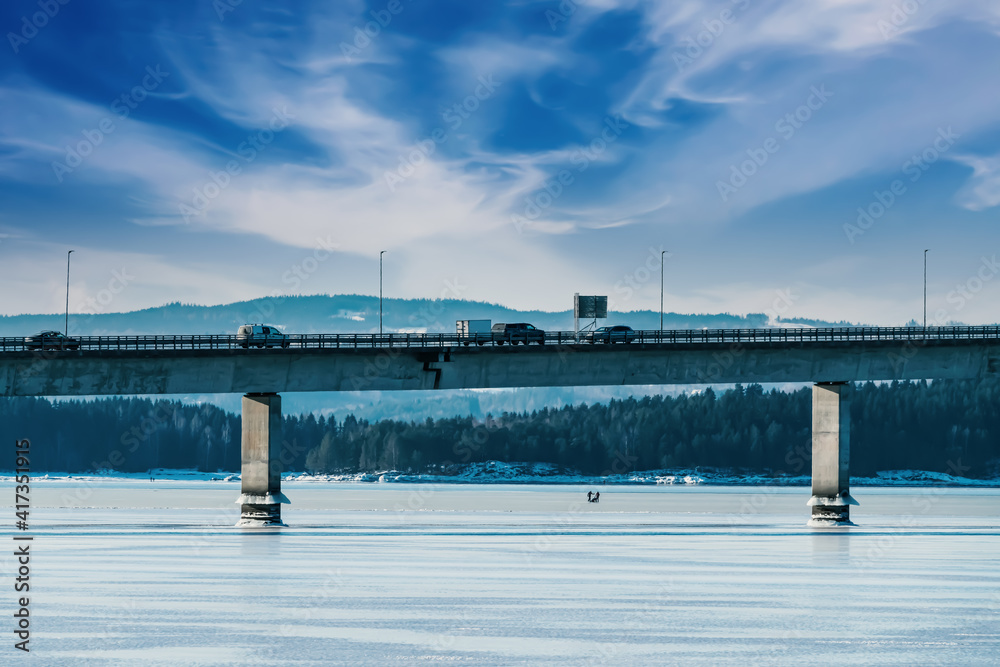 Highway bridge with traffic driving on it, spanning across a frozen bay on a winters day.