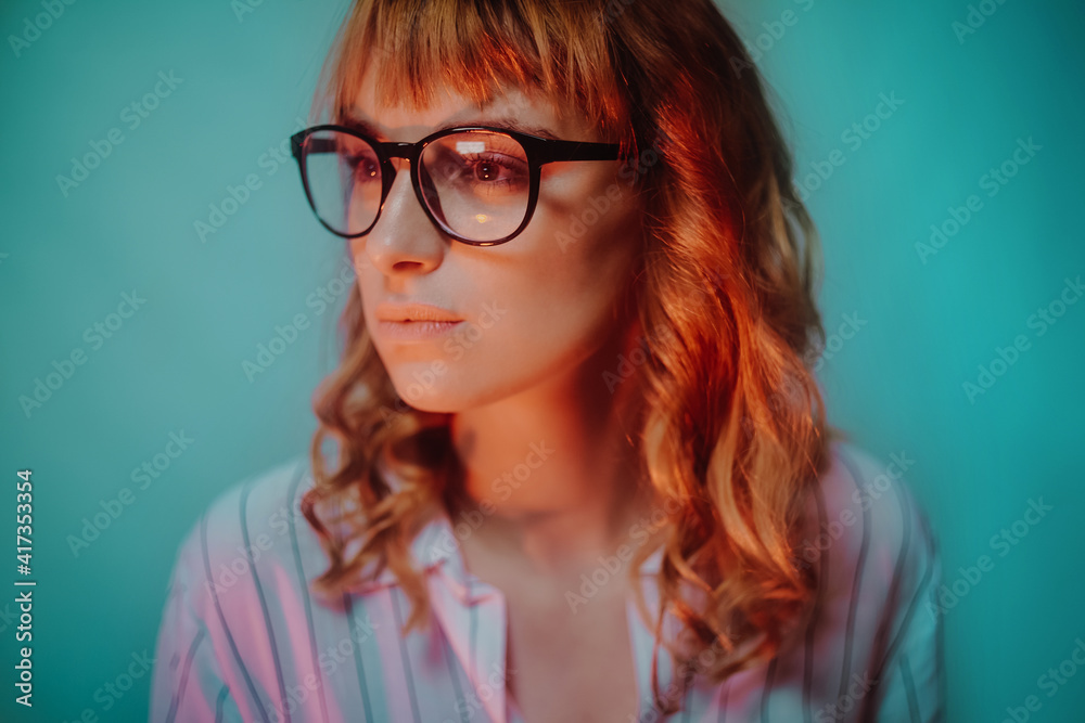 Beautiful girl on a blue background wearing glasses. A student wears glasses in the evening in neon Beautiful girl on a blue background wearing glasses. A student wears glasses in the evening in neon