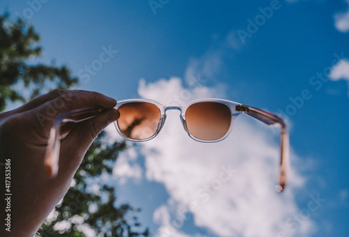 Hand holding sunglasses against sky