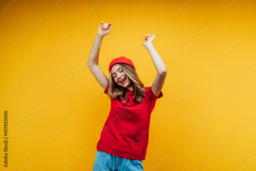 Cheerful young girl dancing on an orange background with space for text. Modern youth, discounts, online shopping Cheerful young girl dancing on an orange background with space for text. Modern youth, discounts, online shopping