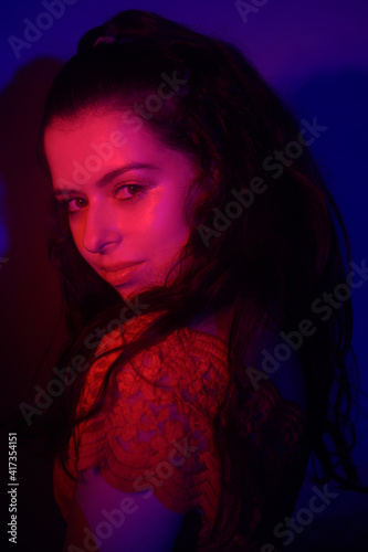 Photo of a woman in neon, beautiful photo in a teen club. Red-blue color. Woman portrait, eye makeup and earrings. Music and dance. Fashion portrait of young elegant