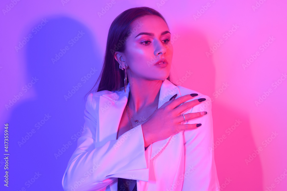Portrait of a gorgeous brunette with big lips, perfect eyebrows, in big earrings, ringlets. A chic girl in a neon light. A party. Girl in a white jacket. Portrait of a gorgeous brunette with big lips, perfect eyebrows, in big earrings, ringlets. A chic girl in a neon light. A party. Girl in a white jacket.