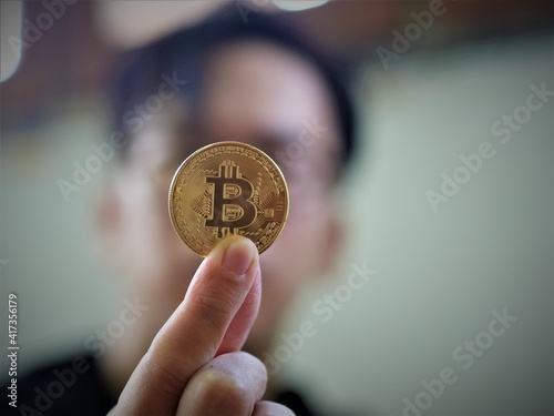 A man hold a golden coin of bitcoin(BTC). A cryptocurrency made by Satoshi Nakamoto