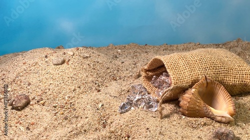 Billede på lærred Crystals falling out of the jute bag on the sand visible stones and shells