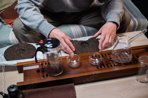 Set for a tea ceremony close-up. A man using a tea needle breaks a tea cake of strong old ripe tea to enjoy the aroma