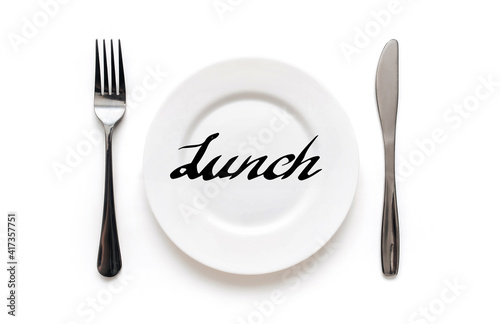 A white plate on which the word Lunch is written standing on a tablecloth . The concept of a balanced diet, ration and medical fasting. Top view, white background, copy space.