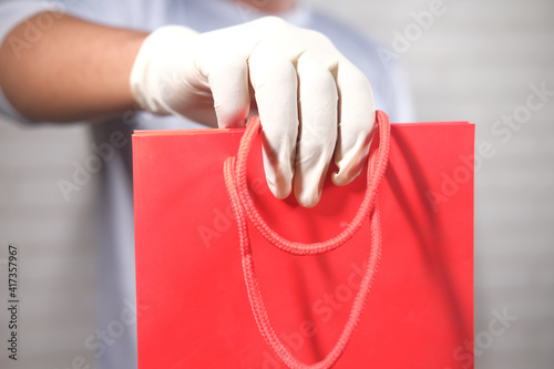 hand in latex gloves holding red color shopping bag on white background 