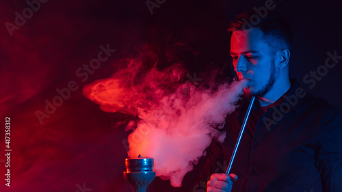 Foto male smoker smokes a hookah and lets out a cloud of smoke