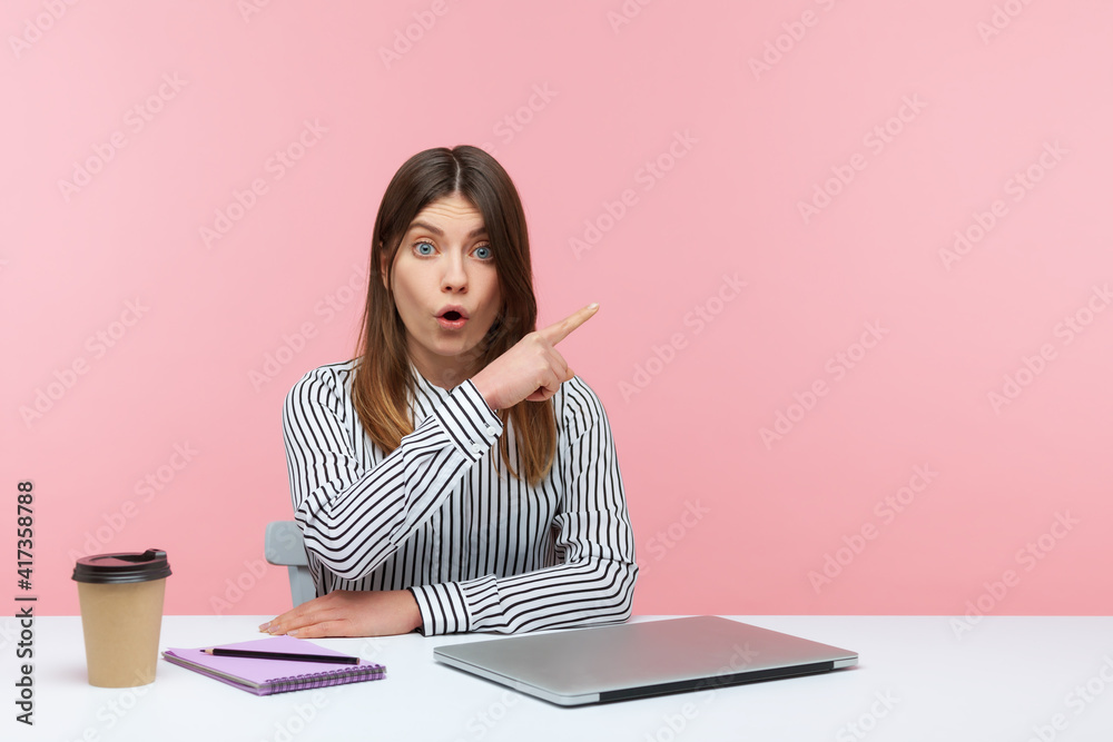 Excited shocked woman pointing finger away paying your attention at empty space for advertising banner, looking at camera with astonishment. Indoor studio shot isolated on pink background Excited shocked woman pointing finger away paying your attention at empty space for advertising banner, looking at camera with astonishment. Indoor studio shot isolated on pink background