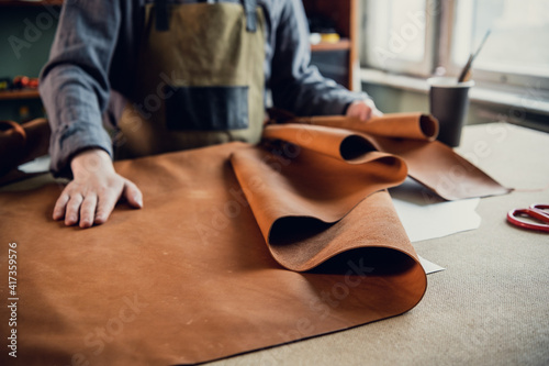 Canvas Print A young apprentice in a boot workshop prepares leather for further use on a large table