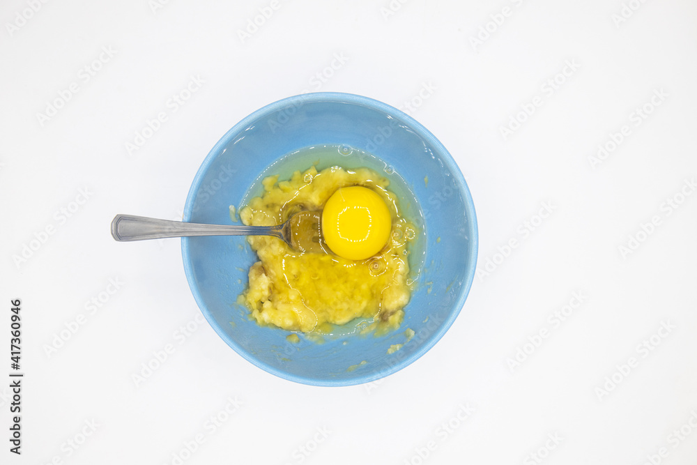 Step 3. Add one egg to banana mixture and mix. Cooking banana pancakes without flour tutorial. Step by step recipe. Top view white background. Gluten free breakfast. Step 3. Add one egg to banana mixture and mix. Cooking banana pancakes without flour tutorial. Step by step recipe. Top view white background. Gluten free breakfast.