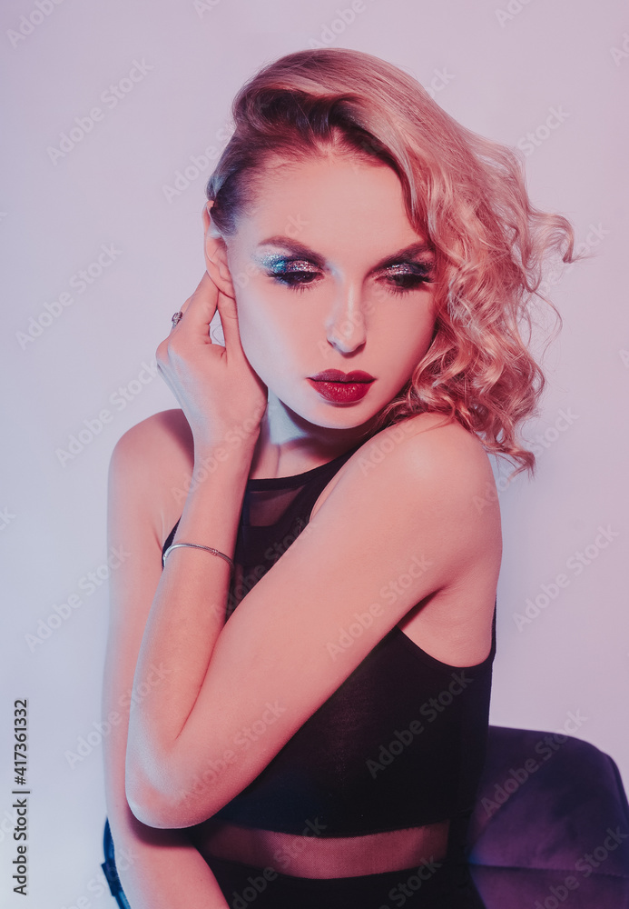 Fototapeta premium Fashion photo of young girl on Colored background, studio shot. Beautiful blond woman with red lips curly hair. Woman in neon light. The girl in body dancing go-go, night club. Sexy swimsuit