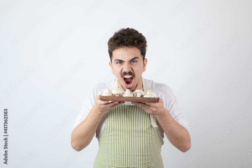 Portrait of hungry male cook holding raw mushrooms on white background Portrait of hungry male cook holding raw mushrooms on white background