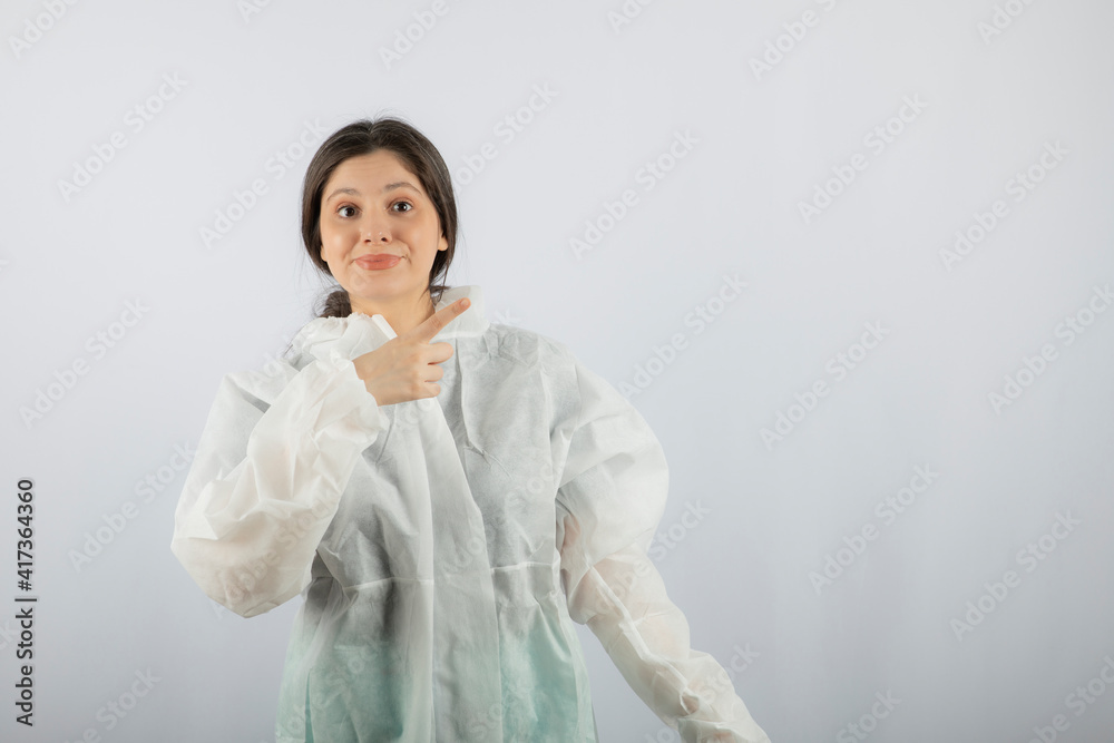 Portrait of young female doctor scientist in defensive lab coat pointing away Portrait of young female doctor scientist in defensive lab coat pointing away