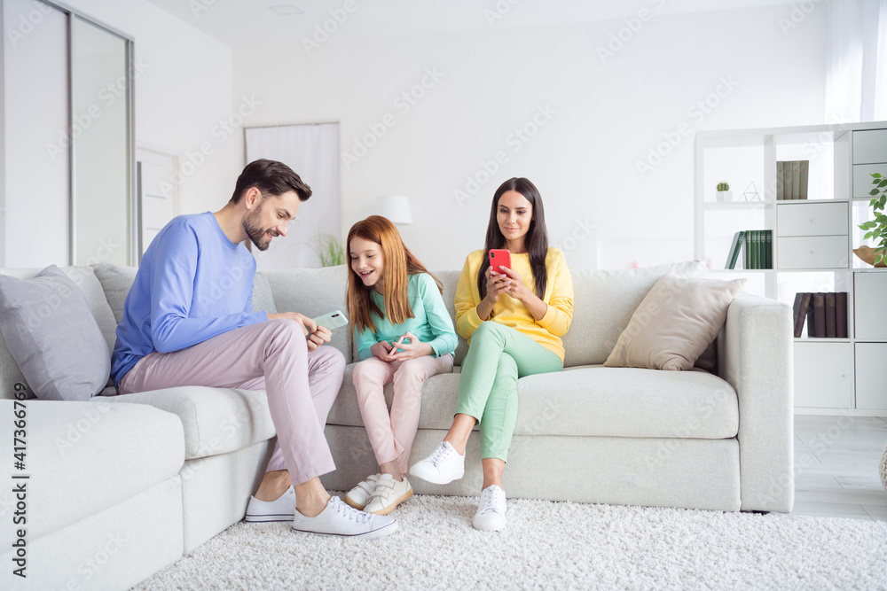 Full length photo of young cheerful family happy positive smile read browse cellphone sit couch home Full length photo of young cheerful family happy positive smile read browse cellphone sit couch home