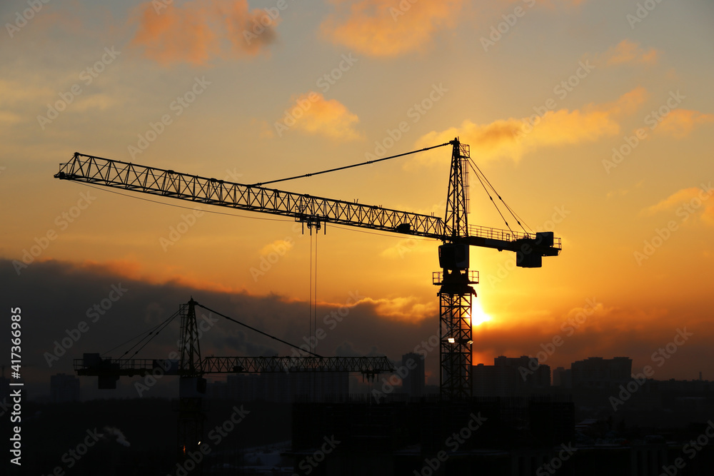 Silhouettes of construction cranes and residential buildings on sunrise background. Housing construction, apartment block in city