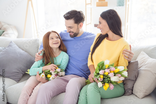 Photo of cheerful family mom dad kid happy positive smile cuddle sit couch flowers bouquet spring indoors