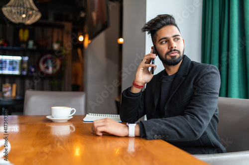 Young handsome indian man talk phone while sitting in cafe shop
