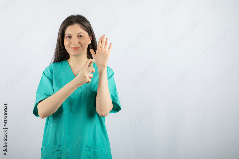 Smiling female nurse spraying her hand on white background Smiling female nurse spraying her hand on white background
