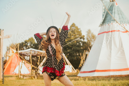 Young beautiful girl smiling on background teepee, tipi- native indian house. Pretty girl in hat with long cerly hair, in dress pouse. Travel in Western. Freedom, smile cute woman. Unusual hotels