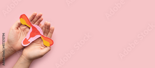Female reproductive health concept. Woman hand holding uterus shape made frome paper on pink background. Awareness of uterus illness such as endometriosis, PCOS, STDs or gynecologic cancer.