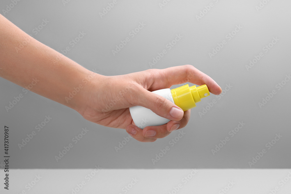 Woman with bottle of insect repellent spray on grey background, closeup Woman with bottle of insect repellent spray on grey background, closeup